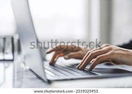 The image captures female hands in close detail, typing on a sleek laptop keyboard, with a fuzzy office setting in the background