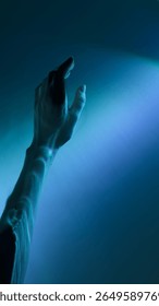 The image captures a hand elegantly reaching out towards a soothing blue light background. This intriguing interplay of light and shadow invites contemplation and imagination.