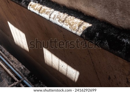 The image captures the interplay of light and shadow on a rough concrete surface, highlighting the textural contrasts made by sunlight.