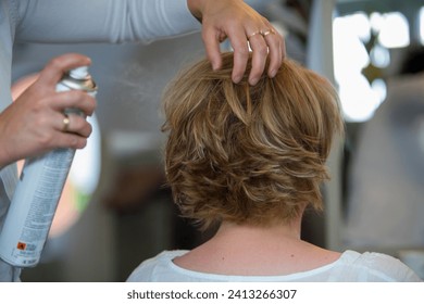 The image captures a moment of hairstyling where hands gently sculpt a short, layered haircut while applying hairspray to set the style in place. The hairstylist's hands are adorned with a wedding - Powered by Shutterstock