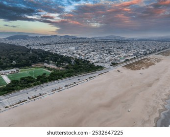 The image captures Ocean Beach in the foreground, Golden Gate Park to the left, and the cityscape of San Francisco under an overcast sky.