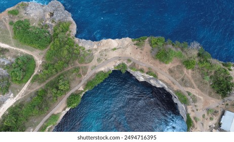 The image captures a stunning aerial view of a coastal landscape with rugged cliffs, clear blue waters, and a winding path, showcasing nature's beauty and serene environment. - Powered by Shutterstock