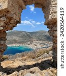 The image captures a stunning vista of a Malvasia coastal town in Greece framed by a weathered stone arch, showcasing a blend of natural beauty and historical architecture.