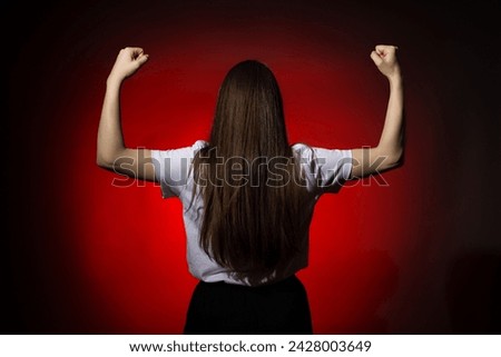 The image captures a woman from behind raising her fists in the air against a red background, signaling victory or defiance.