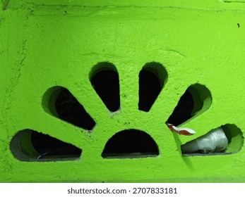Image capturing exterior building texture in bright green paint, showing several rounded slots acting as vents, with visible trash lodged in the openings on the right side.