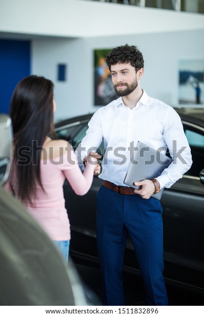 Image of car dealer handshaking with happy female\
in automobile center