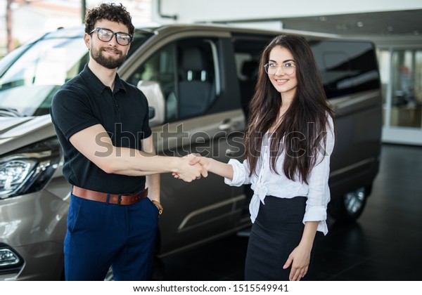 Image of car dealer handshaking with happy female\
in automobile center