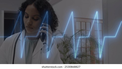 Image of cardiograph over happy biracial female doctor talking on smartphone. Medicine, health and digital interface concept, digitally generated image. - Powered by Shutterstock