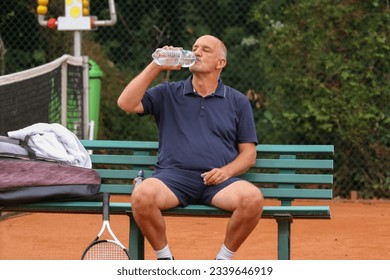 Image of Caucasian middle aged man hydrating drinking water from bottle while tennis game. - Powered by Shutterstock