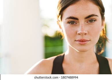 Image of caucasian serious sportswoman looking at camera while working out outdoors