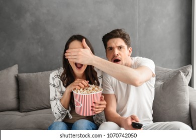 Image Of Caucasian Uptight Family Sitting On Sofa At Home With Popcorn In Hand While Watching Scary Movie