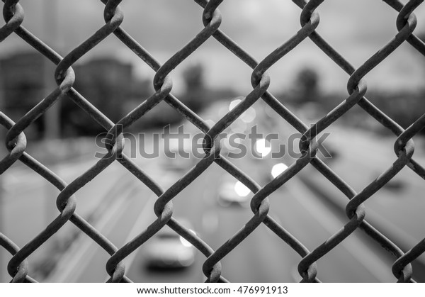 Image of chain link fence on bridge over\
pass. Chain fence on bridge above highway. Abstract industrial\
image of chain link fence and cars on\
highway.