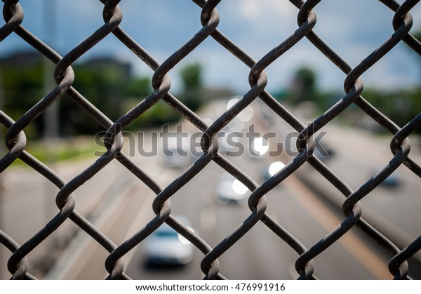 Image of chain link fence on bridge over\
pass. Chain fence on bridge above highway. Abstract industrial\
image of chain link fence and cars on\
highway.
