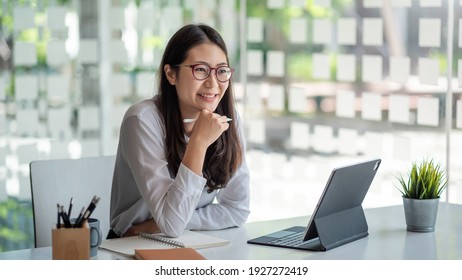 Image of a charming Asian woman working at a modern office. Using a tablet.