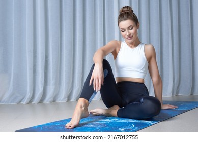 Image of a charming woman in a gymnastic suit sitting on a mat in a bright studio. The concept of fitness, yoga, pilates, stretching. Mixed media