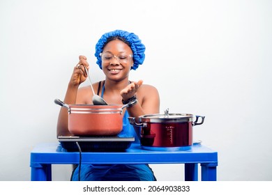 image of cheerful african lady in head wrap, sauce pan, burner on table in front of her- black woman holding ladle- indoor food preparation concept - Powered by Shutterstock