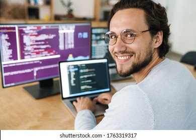 Image of cheerful caucasian programmer man wearing eyeglasses working with computers in office