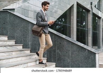 Image of cheerful handsome business man outdoors using mobile phone while going down the stairs - Powered by Shutterstock