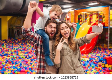 Image of cheerful little child have fun with his parents in entertainment game center. Looking aside make selfie by phone showing peace gesture. - Powered by Shutterstock