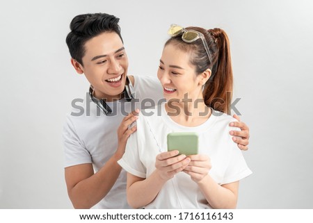 Image of cheerful man smiling while looking at cellphone of his girlfriend isolated overwhite background