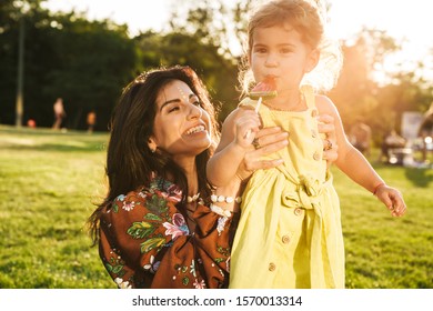 Bild einer fröhlichen, optimistischen jungen Mutter, die sich mit ihrer kleinen Tochter mit Lollipop draußen im Naturpark amüsiert.
