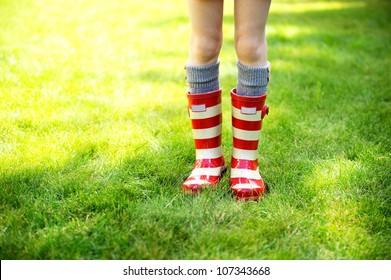 Image Of Child Legs On A Green Lawn Wearing Red Striped Rain Boots