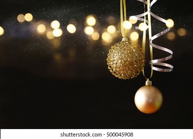 Image of christmas festive tree gold ball decoration in front of black background. Glitter overlay