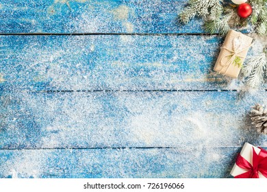 Image For Christmas Greeting Cart. Frozen Furry Spruce On Blue Wooden Table With Snow. Rustic Style. Top View, Copy Space. Little Boxes With Gifts, Cone, New Year Toys.