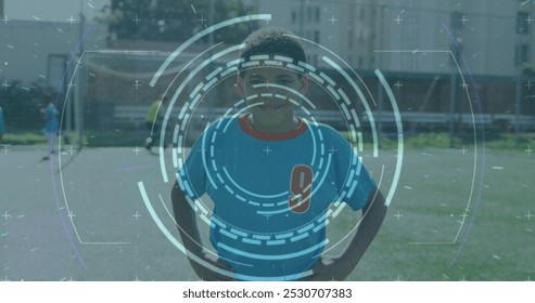 Image of circular scanner processing data over biracial boy in football strip on pitch. Sport, fitness, technology and digital interface concept digitally generated image.