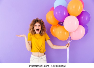 Image closeup of attractive delighted woman rejoicing while posing in multicolored air balloons isolated over violet background