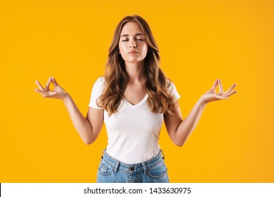 Image Closeup Of Calm Concentrated Woman Wearing Basic T-shirt Meditating With Closed Eyes And Zen Fingers Isolated Over Yellow Wall