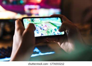 Image Closeup Of Focused Man Playing Video Game On Mobile Phone And Computer At Home