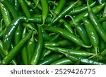 The image is a close-up of a pile of green chillies, showcasing their vibrant color and fresh appearance. Close-up top view of freshly harvested green chillies, displayed in a market places for sale.