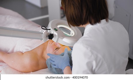 Image Of Closeup Of Woman In Cosmetic Cabinet Under Lamp. Faces Skin Cleaning. Medical Officer Examines The Skin