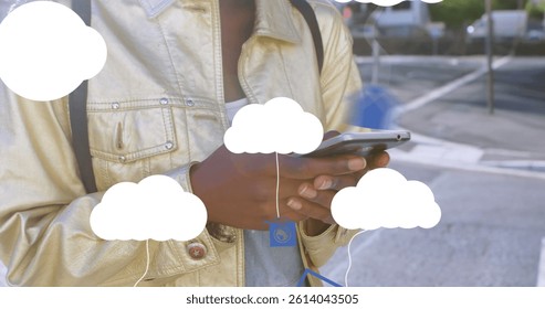 Image of clouds with electronic devices over african american woman using smartphone. global cloud computing, digital interface and data processing concept digitally generated image.