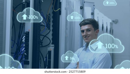 Image of clouds with increasing numbers over smiling caucasian man standing at servers. cloud computing, data uploading, computers and technology concept digitally generated image.