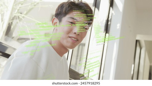 Image of computer language over smiling asian man sitting on chair at home. Digital composite, multiple exposure, business, coding, programming language, close up and technology concept.