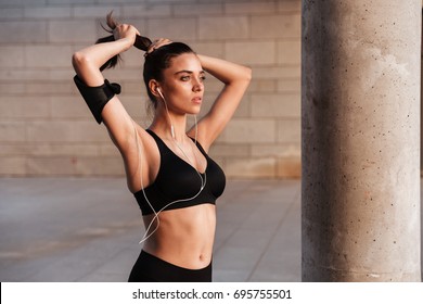 Image of concentrated young sports lady standing with earphones outdoors.