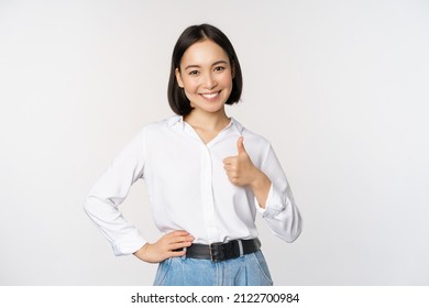 Image of confident asian woman showing thumb up in approval, recommending, like smth good, standing over white background