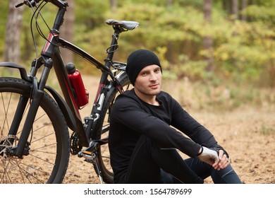 Image of confident handsome model posing over bicycle background, relaxing and enjoying free time, being in for sport, breathing fresh air, looking directly at camera, having rest around nature.