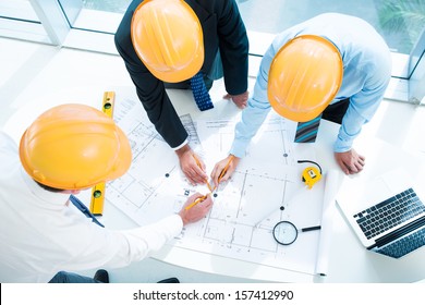 Image of constructor workers sketching together on the foreground viewed below