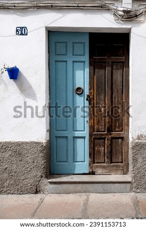 The image contrasts two Cordoba doors: a freshly painted blue one on the left and an aged, weathered wooden door on the right, with tangled cables above and a blue flower pot adding color.