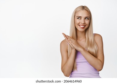 Image of coy blond girl smiling, rubbing hands and looking cunning, thinking of something, evil genius face, standing over white background