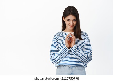 Image of cunning young woman has plan, steeple fingers and smiling like evil genius, thoughtful smirk, scheming devious plan, standing over white background