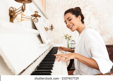 Image of a cute cheerful positive lady in white shirt play the piano indoors at home. - Powered by Shutterstock