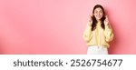 Image of cute cheerful woman cross her fingers for good luck and looking hopeful at camera, making wish, standing over pink background.