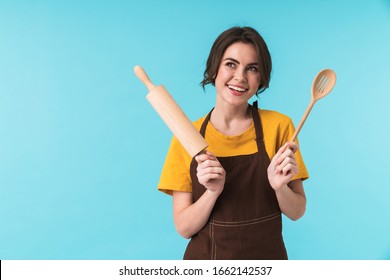 Image of cute happy young woman chef holding rolling pin and wooden spoon isolated over blue wall background. - Powered by Shutterstock