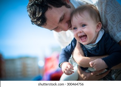 Image Of Cute Little Daughter In Young Dad's Hands. Father And Baby Girl Outdoor. Child Plays On Playground.