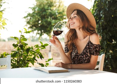 Image of cute pretty young woman sitting in cafe outdors in park with book holding glass drinking wine. - Powered by Shutterstock