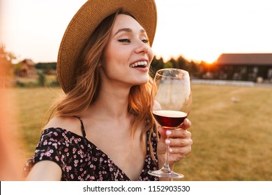 Image of cute pretty young woman outdoors holding glass drinking wine make a selfie by camera.